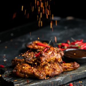 Delicious spicy chicken wings with chilies and spices on dark background.