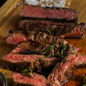 Close-up of sliced grilled steak with seasoning on a wooden board, highlighting texture and juiciness.