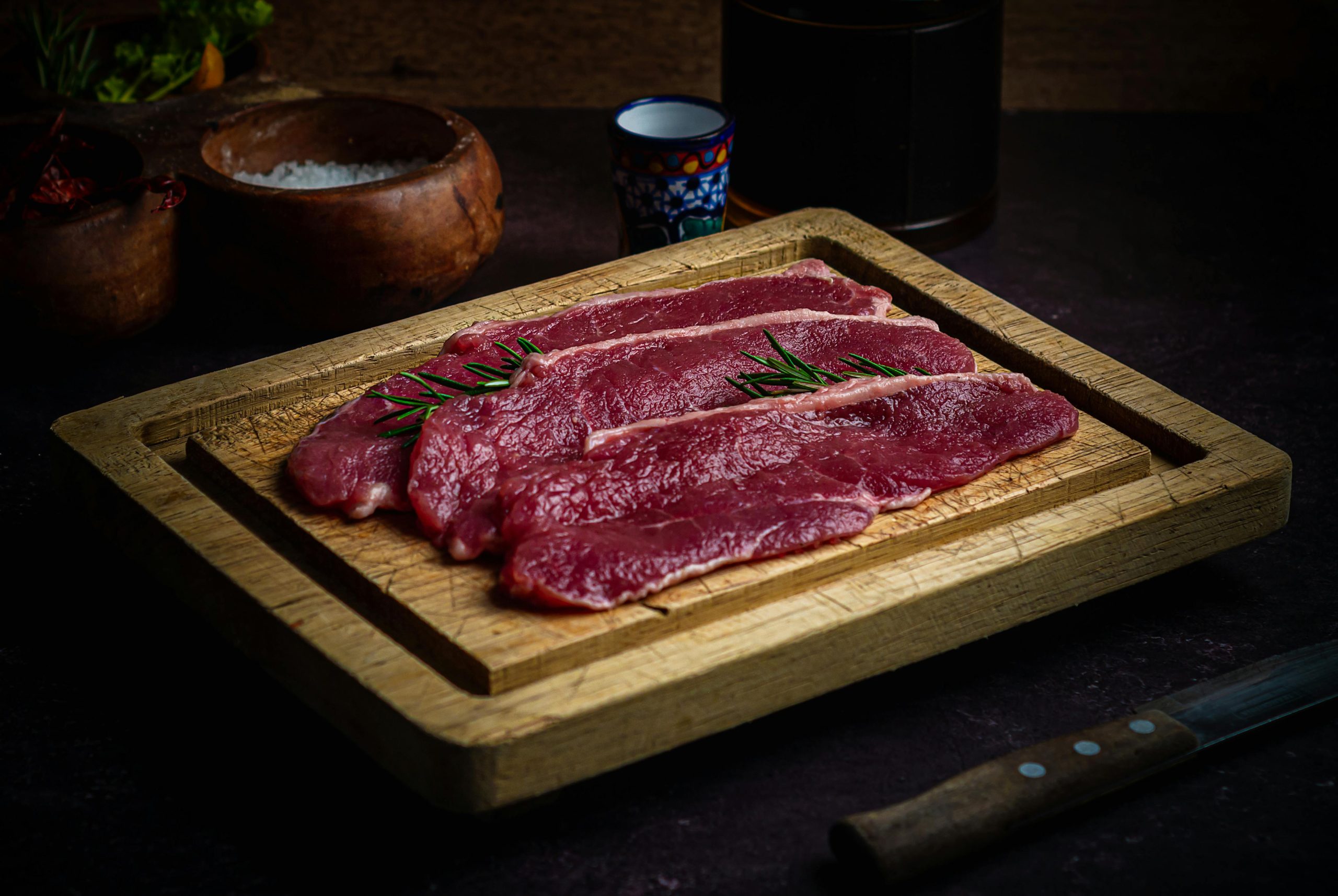 High-quality beef slices garnished with rosemary on a wooden board, perfect for culinary photography.