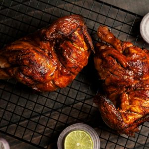 Juicy grilled chicken halves on a cooling rack, garnished with sliced lemon and red onions.